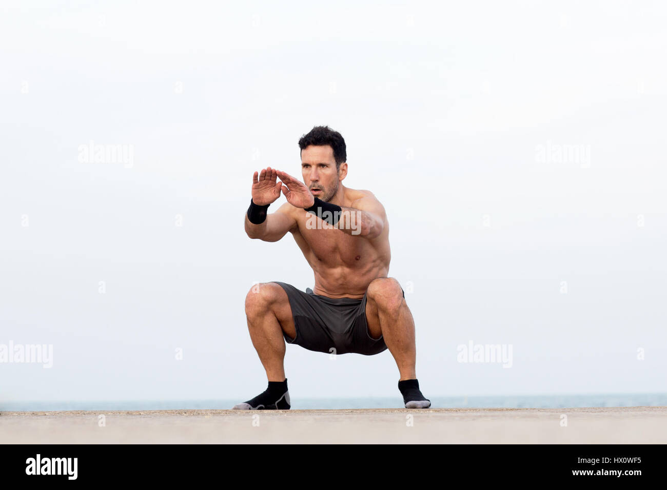 Athletic man makes squats by the sea Stock Photo