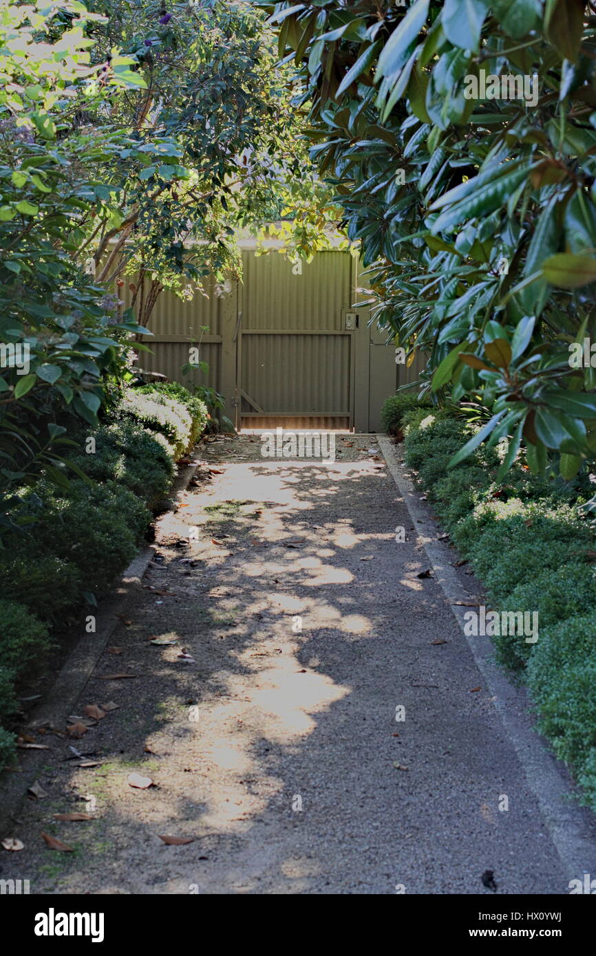 Shaded path with sunny spots and greenery overhead, gate at the end of the path. Stock Photo