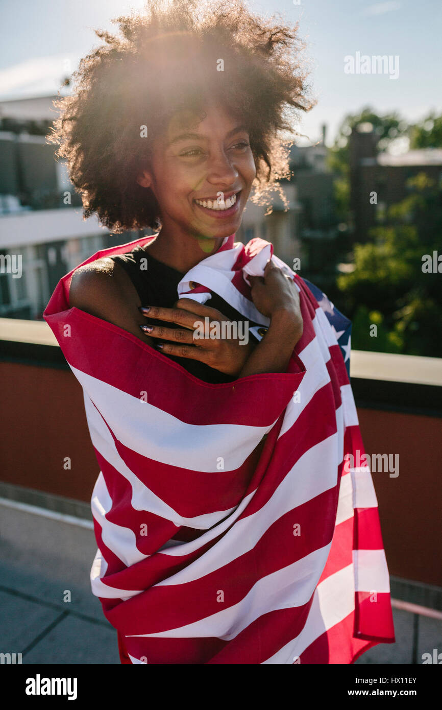 Young woman standing on rooftop warpped in US American flag Stock Photo