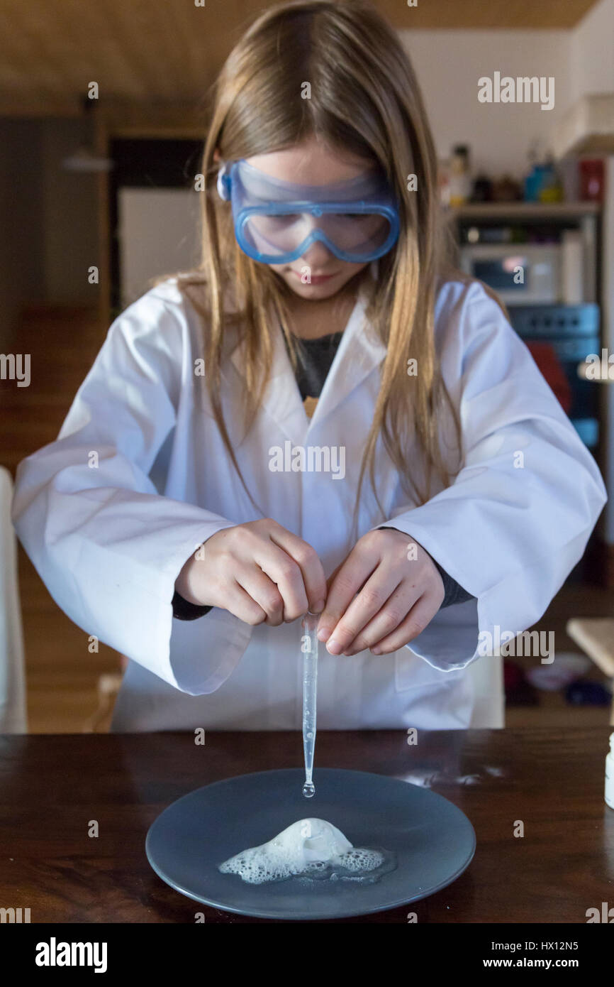 Girl wearing work coat and safety glasses using chemistry set at home Stock Photo