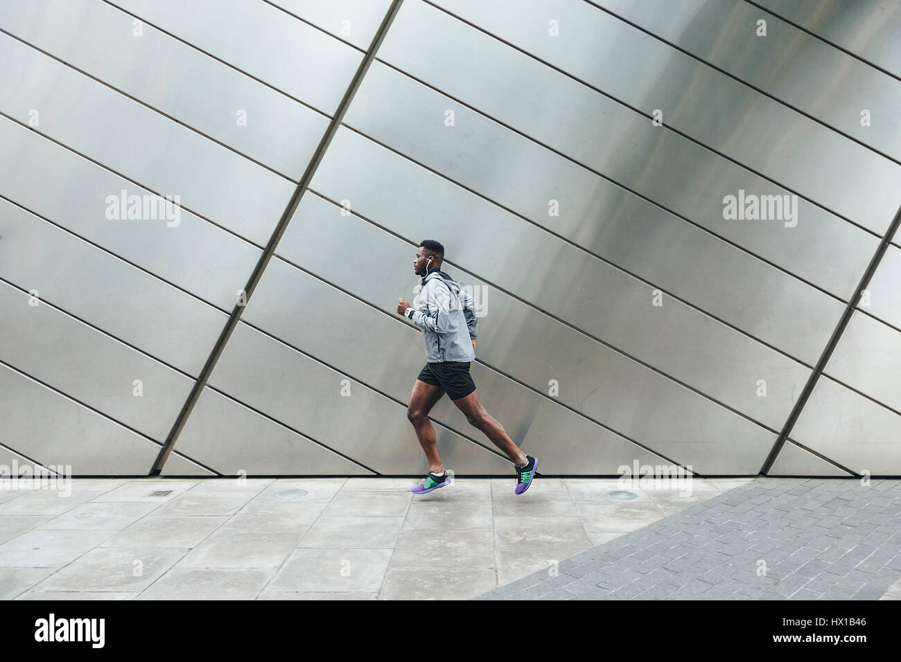 Young man running along building front Stock Photo
