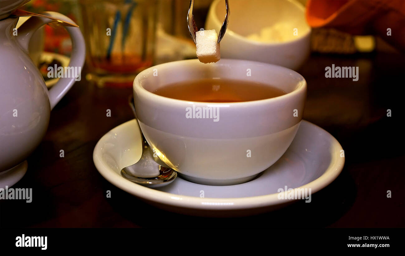 Adding lump sugar with pincers to black tea in cup Stock Photo