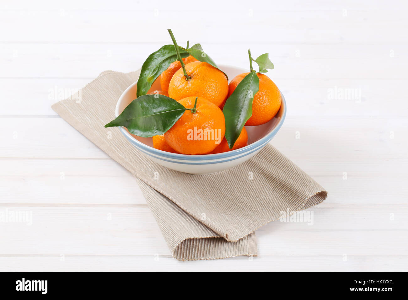 bowl of fresh tangerines with leaves on beige place mat Stock Photo
