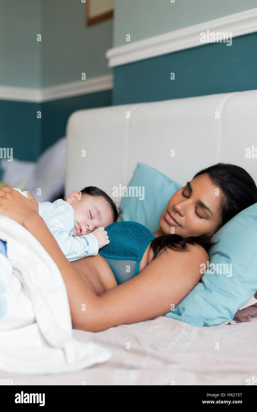 Young mother having a nap in bed with her baby son sleeping on her