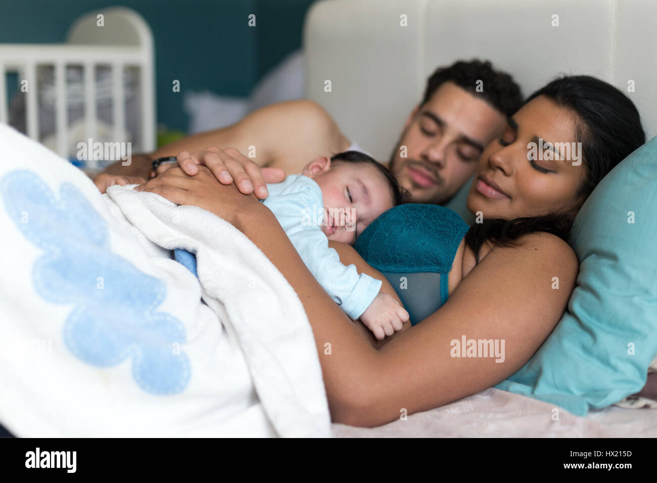 Young couple asleep in bed with their baby son sleeping on his mothers chest. Stock Photo