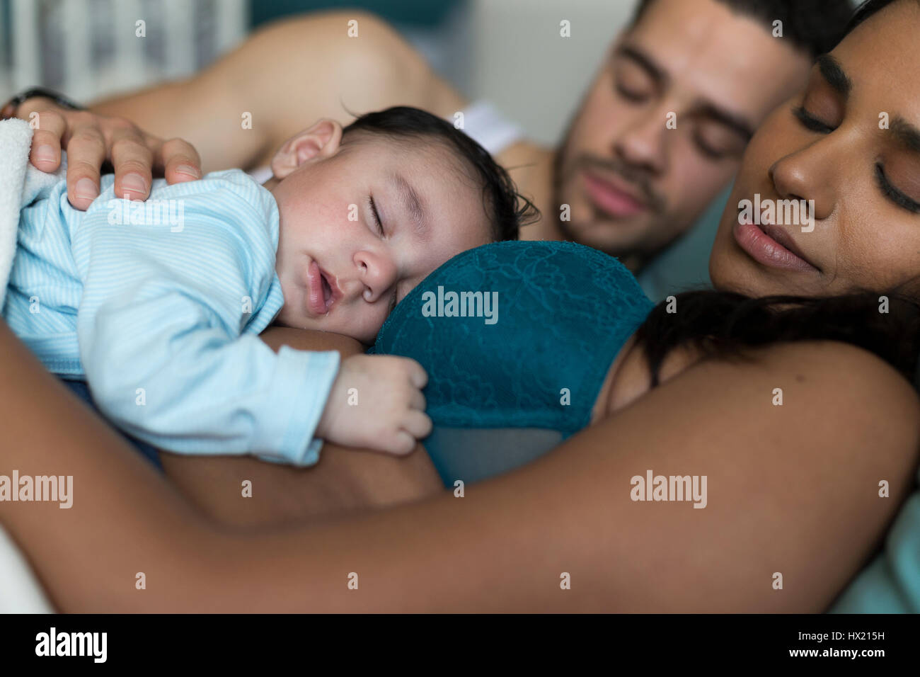 Young couple asleep in bed with their baby son sleeping on his mothers chest. Stock Photo