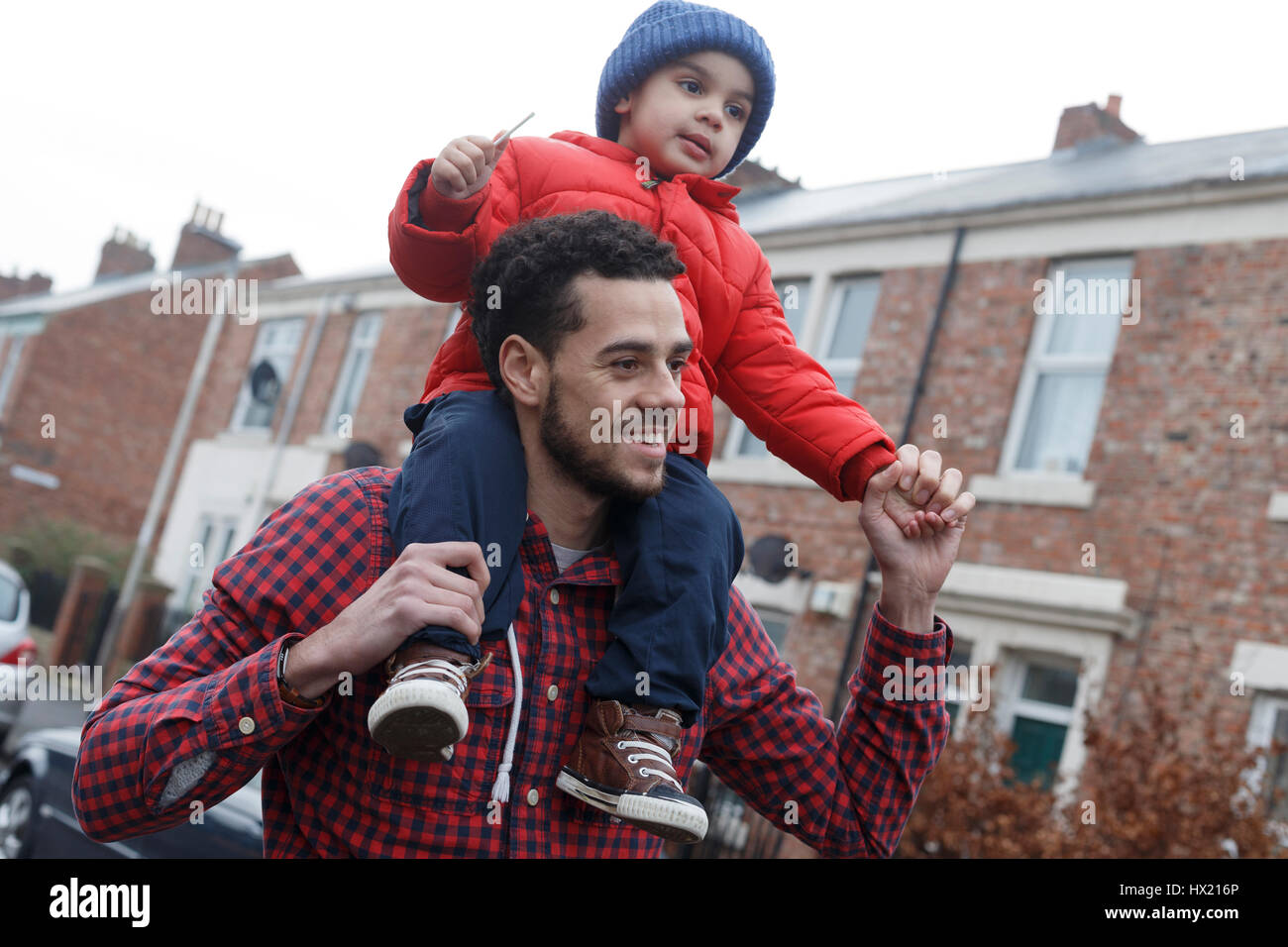 Young father carrying his son on his shoulders as he walks down the street Stock Photo