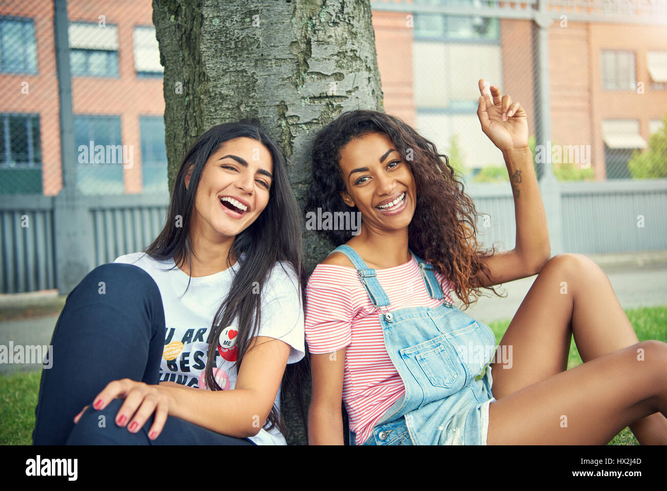 Two laughing friends sitting beside each other with a large tree trunk