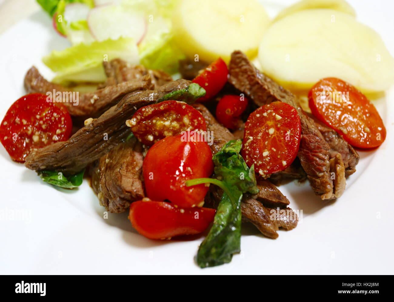 Italian style steak strips with basil and cherry tomatoes, side view Stock Photo