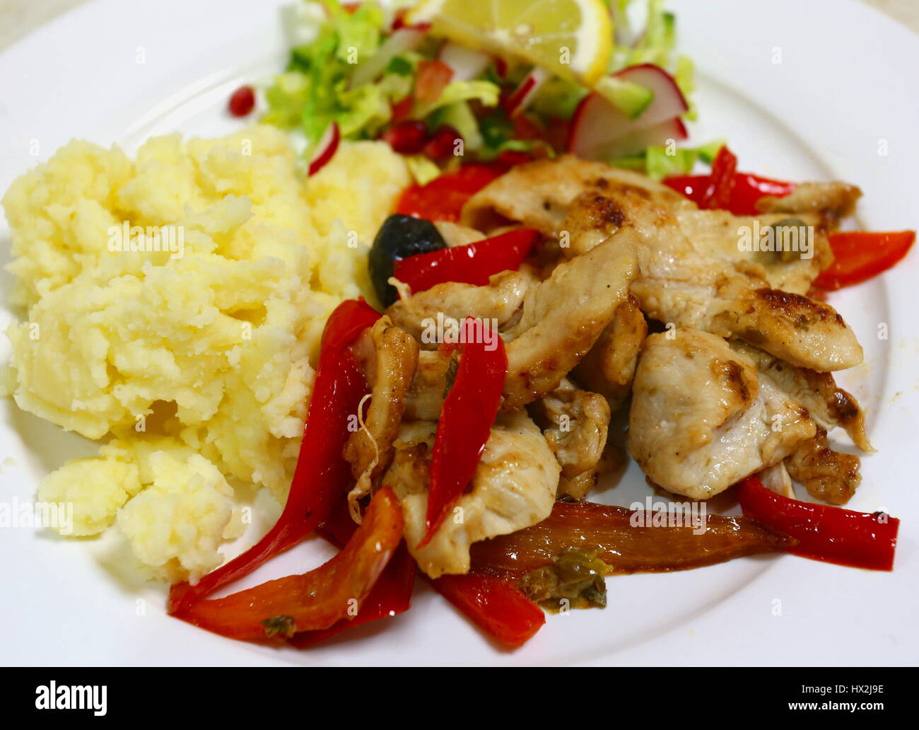 Stir fried chicken tenders and red capsicum slices cooked with olives and capers and served with mashed potato and a chopped salad Stock Photo