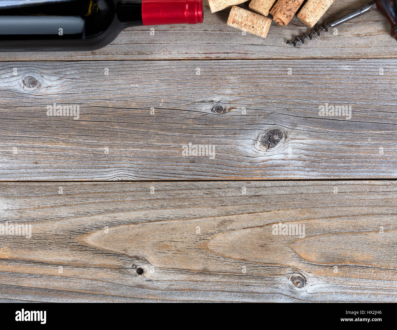 Overhead view of a top border of partial red wine bottle, corks and vintage corkscrew on rustic wood Stock Photo