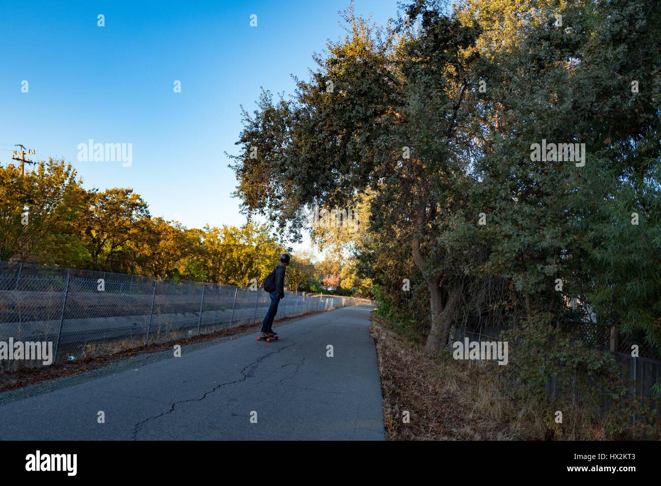 A teenager wearing a helmet rides a skateboard down a path on the Contra Costa Canal Trail, Walnut Creek, California, October 19, 2016 Stock Photo