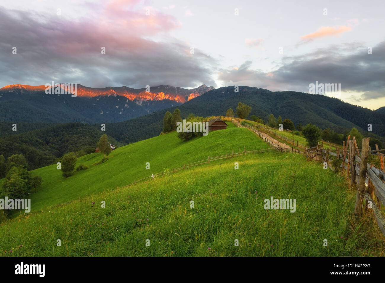 Beautiful sunset with green fields and sunlit mountain range in the background photographed in Transylvania near Brasov on a beautiful hilly setting Stock Photo