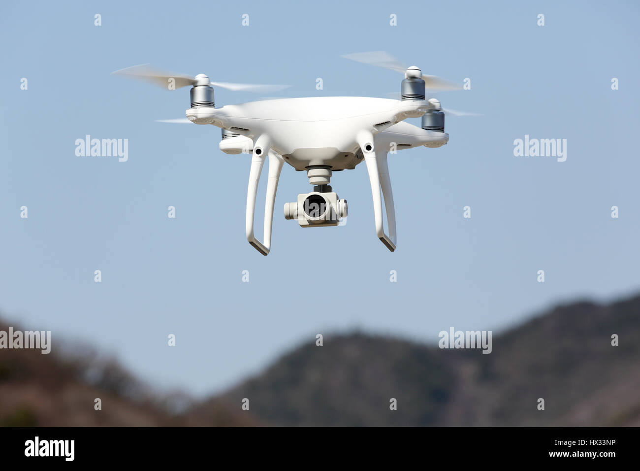 White remote controlled Drone Dji Phantom4 Pro equipped with high resolution video camera hovering in air and blue sky in the background Stock Photo