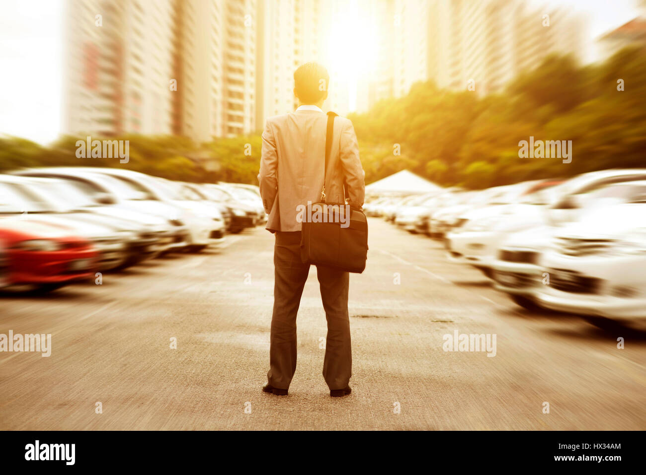 Rear view businessman standing at open car park, looking away with beautiful sunlight. Stock Photo