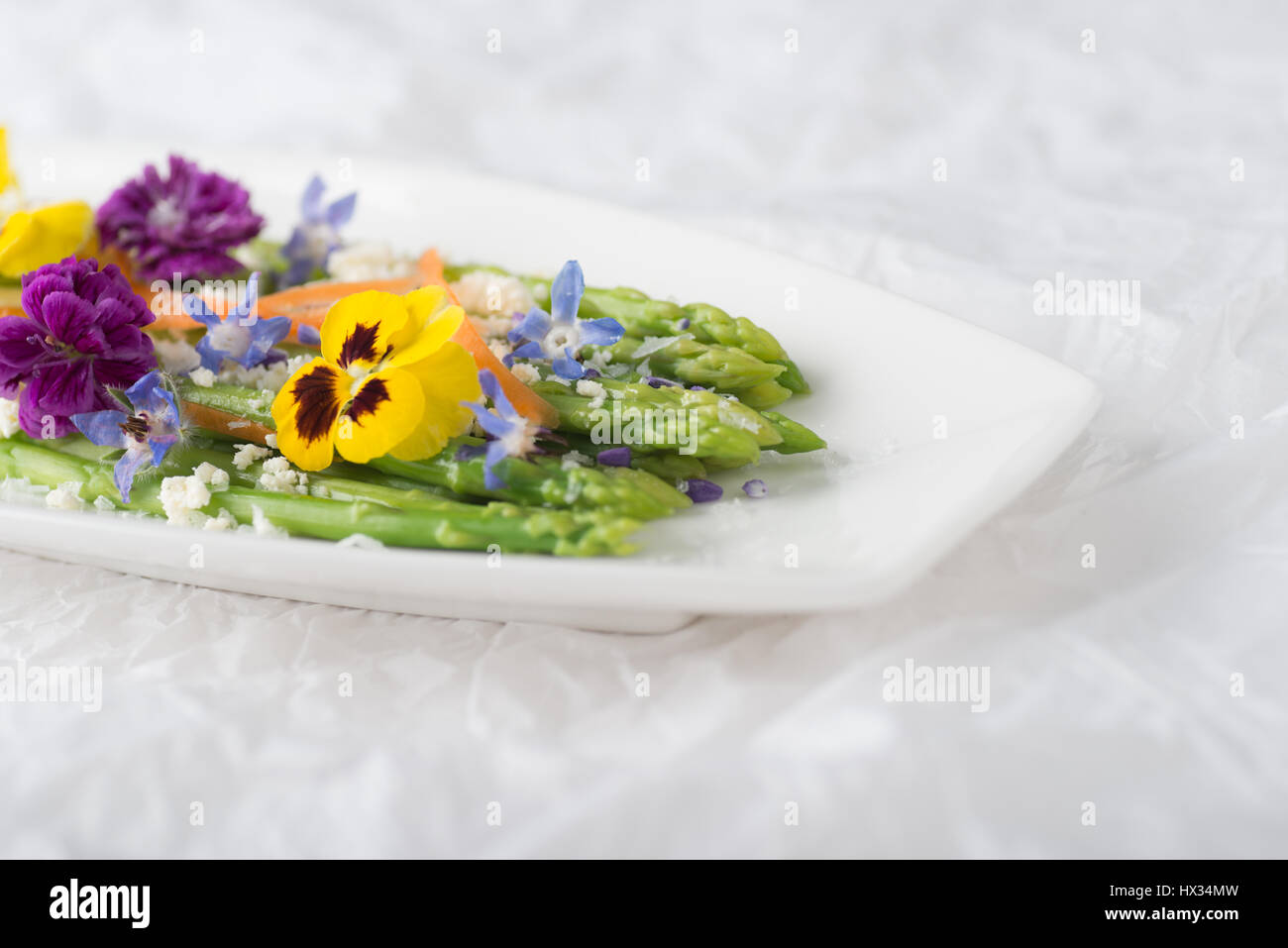 Baby asparagus with feta cheese and edible flowers in white environment