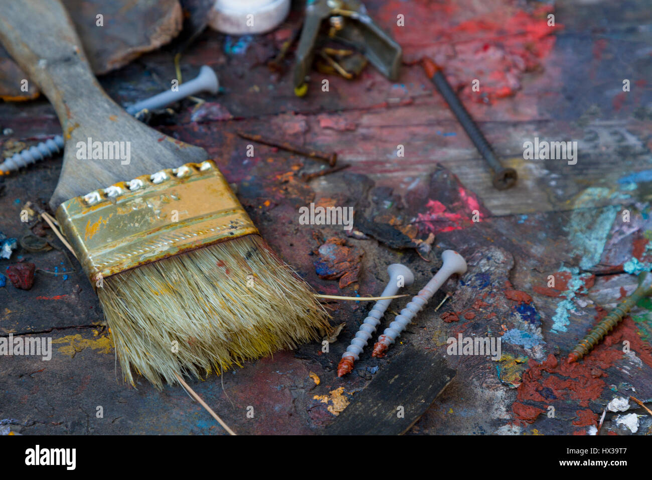 Messy disarray with old paint brush and paint daubed screws on wood with bits of oil colors.  Well-worn, discarded painting tools. Stock Photo