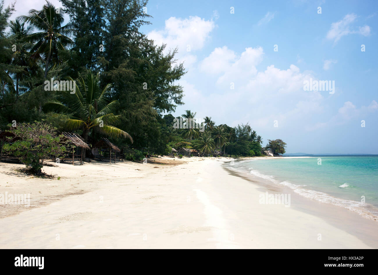 Tropical stretched out white sand beach and palm trees with blue colored ocean seashore water in the afternoon at Tanjung Pinang on Bintan island, Ind Stock Photo