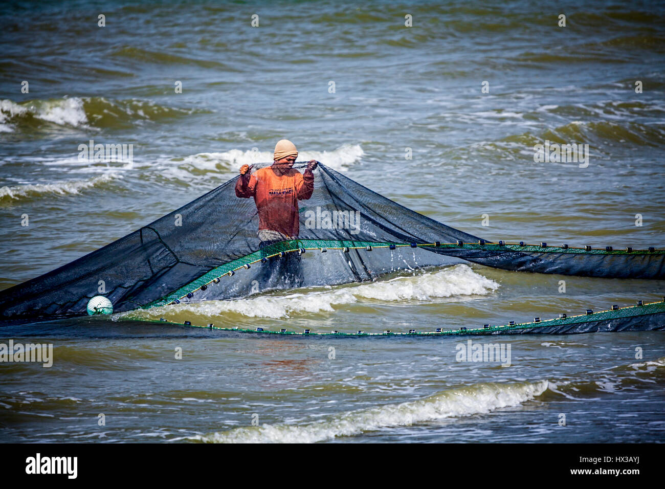A young Filipino fisherman works with his seine net in surf close to shore at Baybay Beach, Roxas City, Panay Island, Philippines, Southeast Asia. Stock Photo