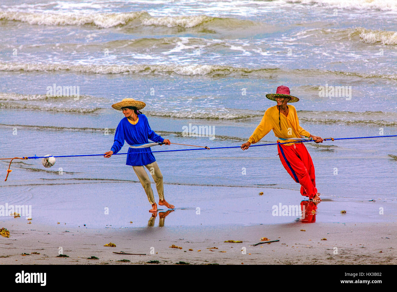 Colorfully dressed Filipinos haul their seine net to shore in the Philippines. Stock Photo