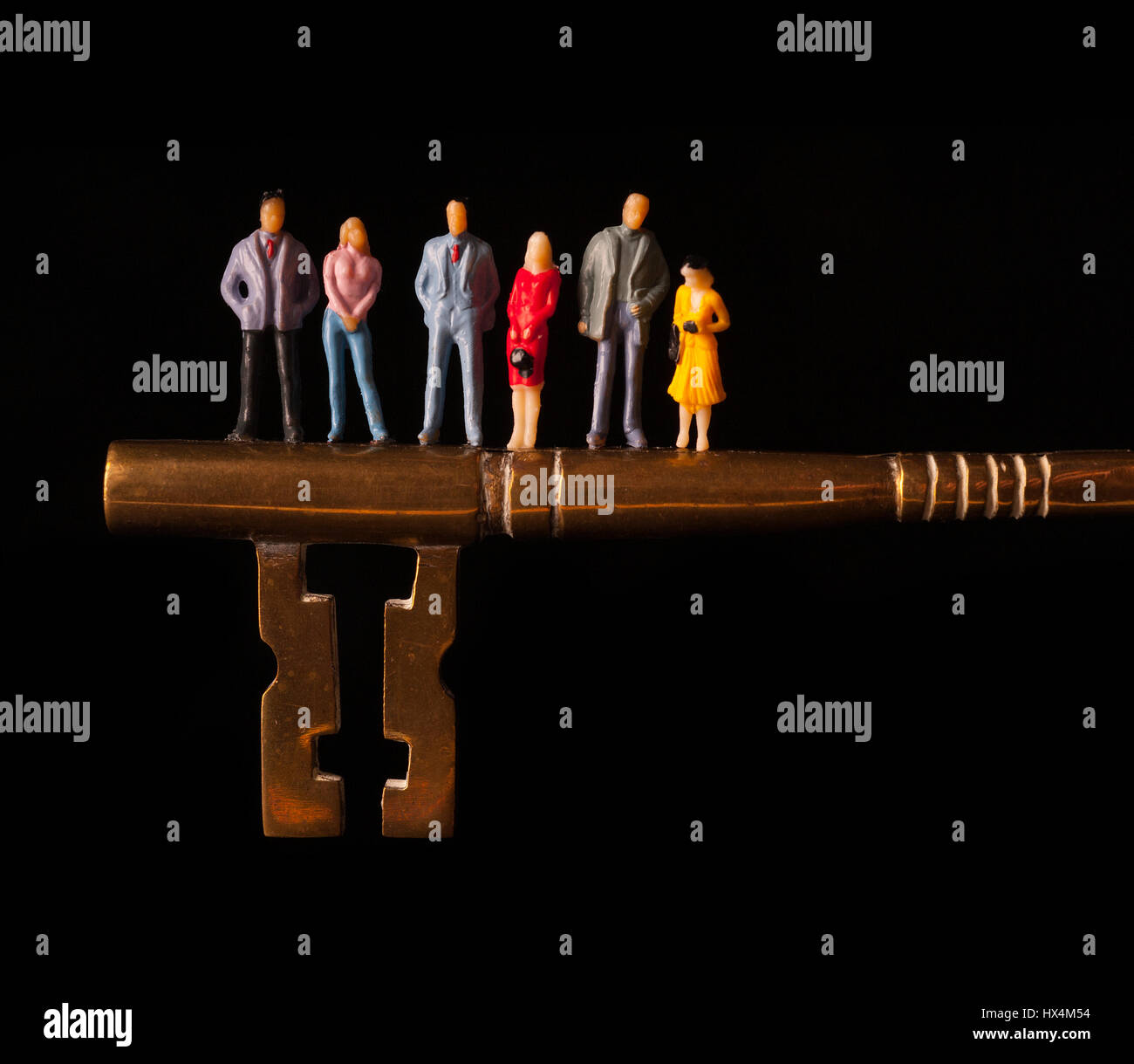 Group of miniature figures standing on giant brass key against black background Stock Photo