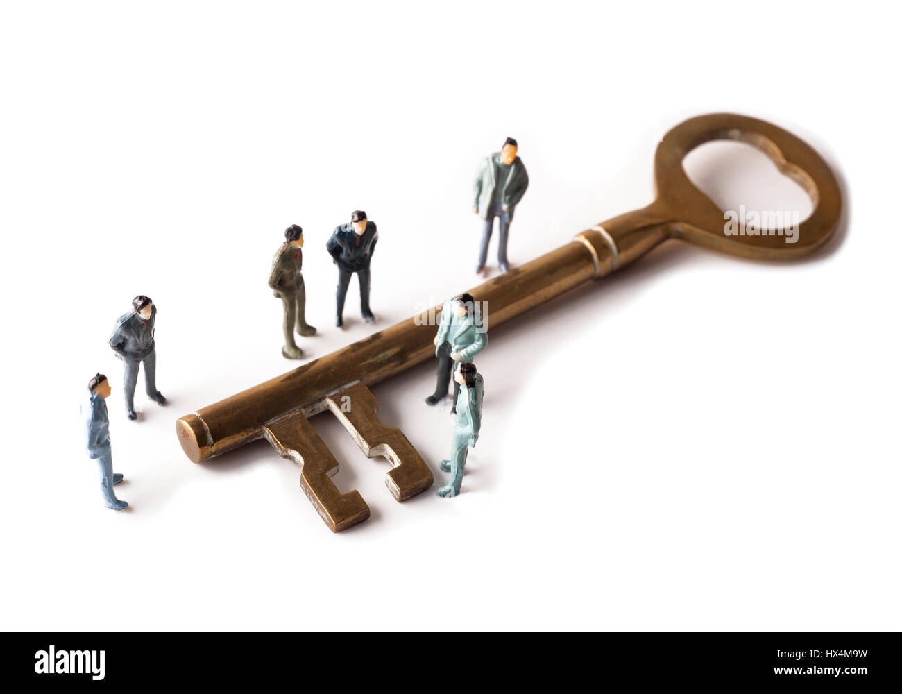 Group of miniature figures standing around giant brass key on white background Stock Photo