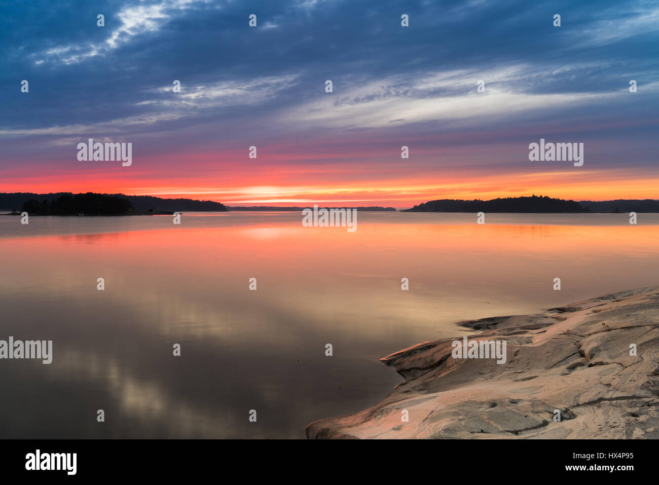 THE SWEDISH FINNISH ARCHIPELAGO IN THE BALTIC SEA AT SUNSET OR SUNRISE WITH RICH COLOURS AND ROCKS IN THE FOREGROUND WITH REFLECTIONS Stock Photo