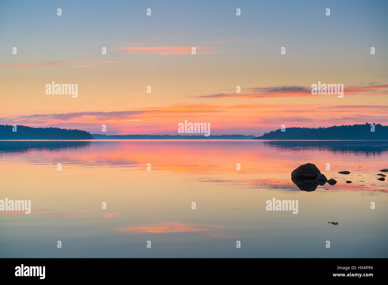 THE SWEDISH FINNISH ARCHIPELAGO IN THE BALTIC SEA AT SUNSET OR SUNRISE WITH RICH COLOURS AND ROCKS IN THE FOREGROUND WITH REFLECTIONS Stock Photo