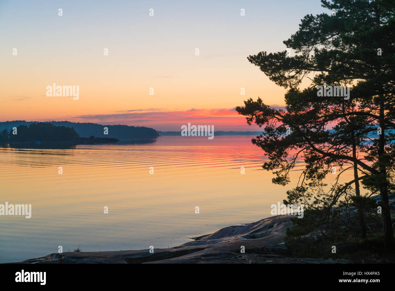 THE SWEDISH FINNISH ARCHIPELAGO IN THE BALTIC SEA AT SUNSET OR SUNRISE WITH RICH COLOURS AND AN ISLAND SILHOUETTED IN THE FOREGROUND Stock Photo