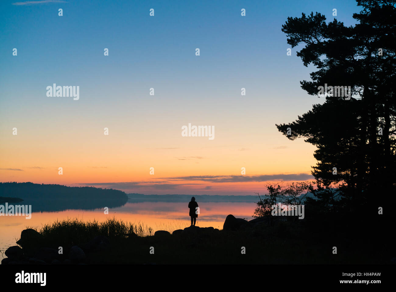 THE SWEDISH FINNISH ARCHIPELAGO IN THE BALTIC SEA AT SUNSET OR SUNRISE WITH RICH COLOURS A PERSON AND ISLAND SILHOUETTED IN THE FOREGROUND Stock Photo