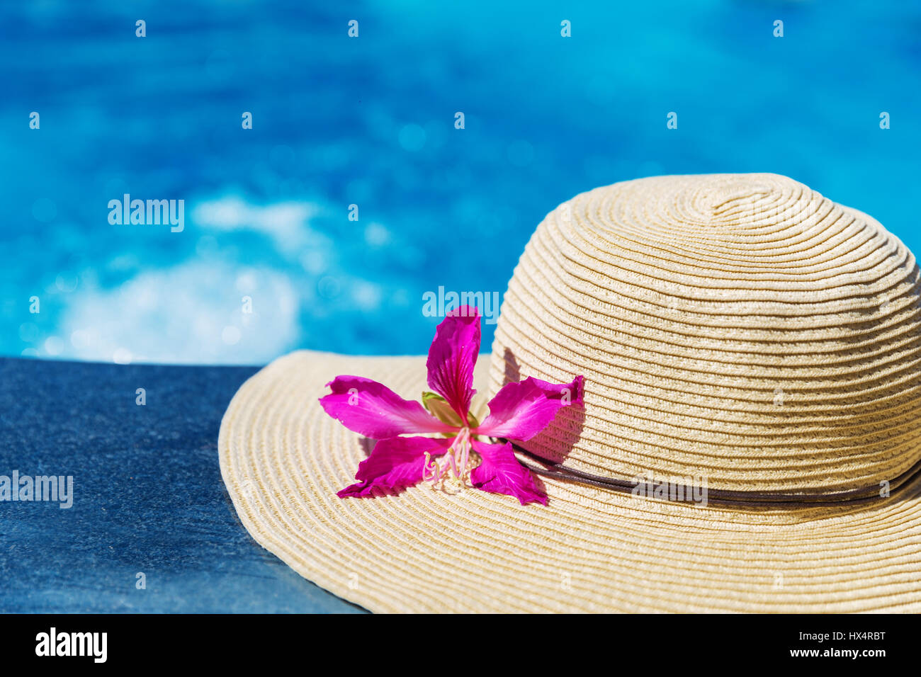 Straw hat with orchid flower and blue towel near swimming pool ...