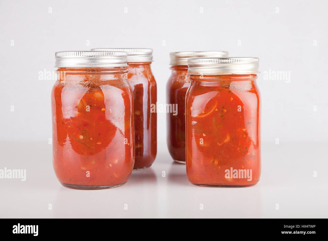 Jars of homemade cooked spaghetti sauce on a white surface. Food cans