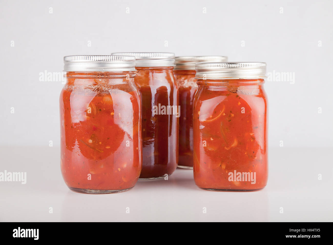 Jars of homemade cooked spaghetti sauce on a white surface. Food cans