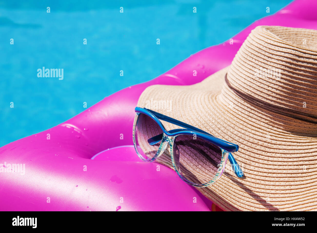Sunglasses and straw hat on a pink air mattress in swimming pool. Tropical summer concept. Stock Photo