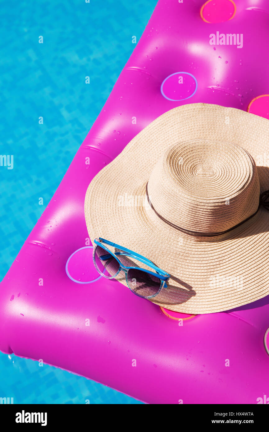 Sunglasses and straw hat on a pink air mattress in swimming pool. Tropical summer concept. Stock Photo