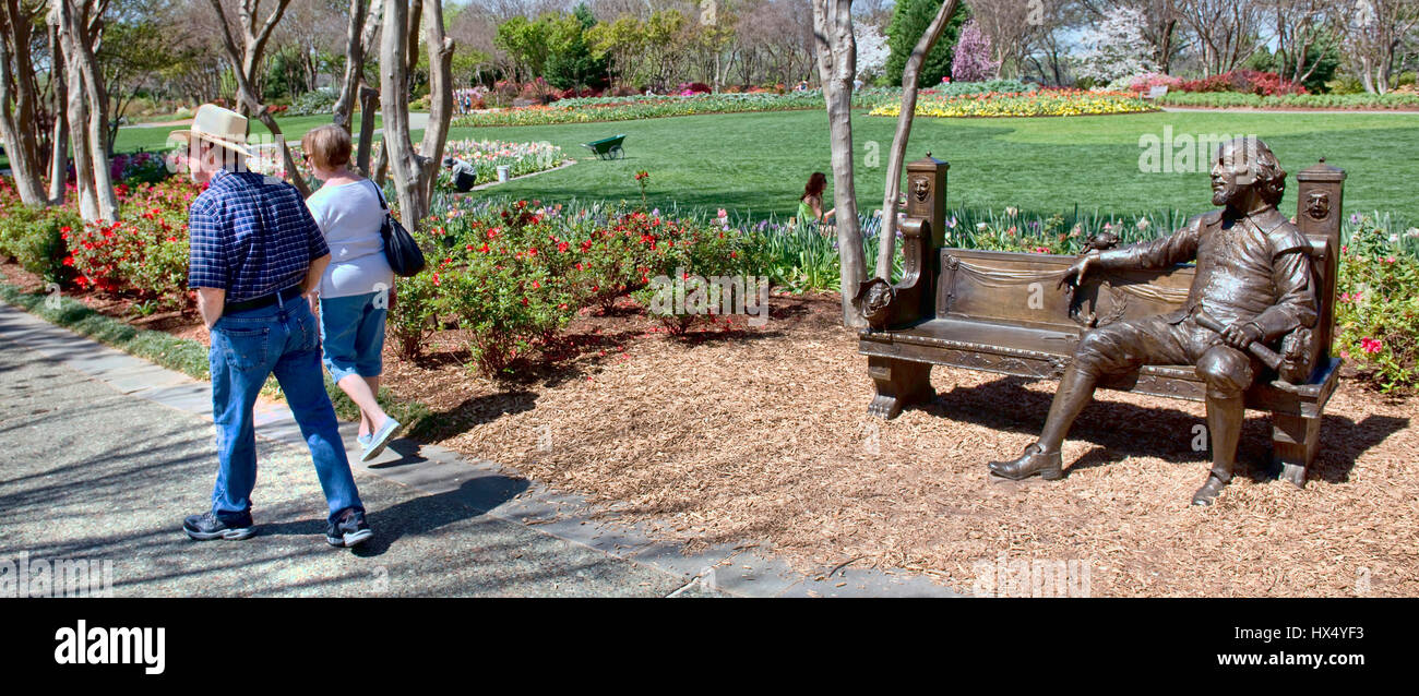 Dallas, Texas - March 22, 2017  Couple taking a Spring day walk at the Dallas Arboretum with a bronze Shakespeare statue watching them. Stock Photo