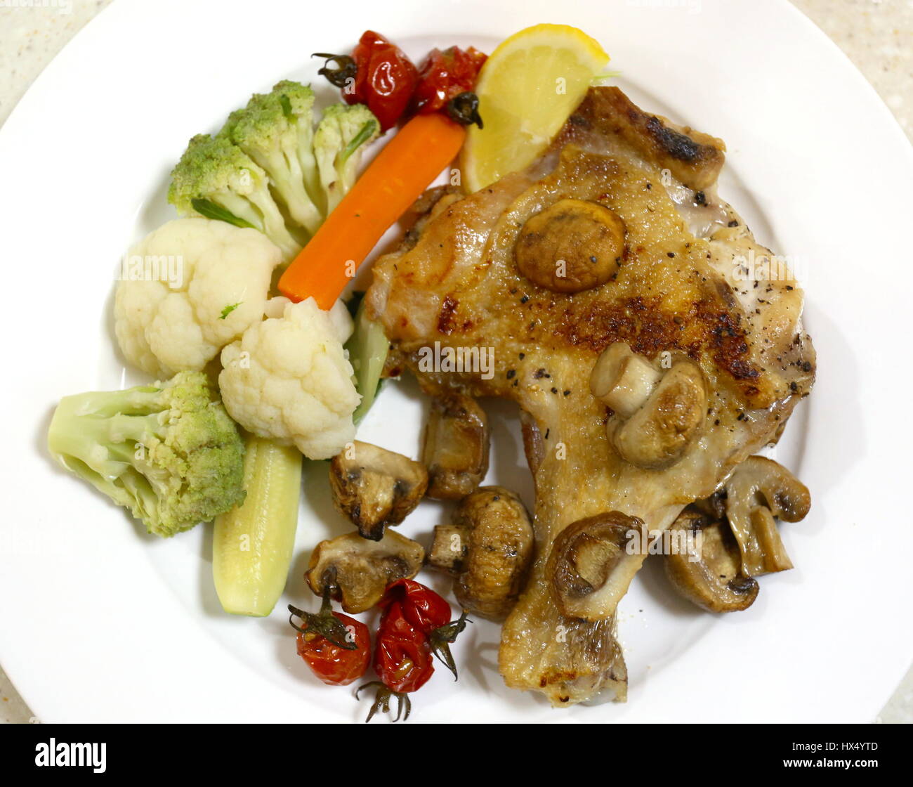 Oven grilled chicken leg and mushrooms, served with steamed cauliflower, courgette,carrot, cherry tomatoes and romanesco broccoli. Stock Photo