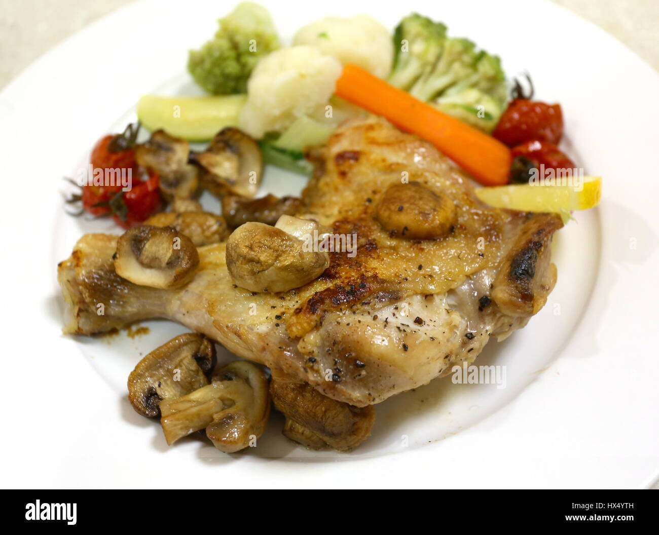 Oven grilled chicken leg and mushrooms, served with steamed cauliflower, courgette,carrot, cherry tomatoes and romanesco broccoli, Stock Photo