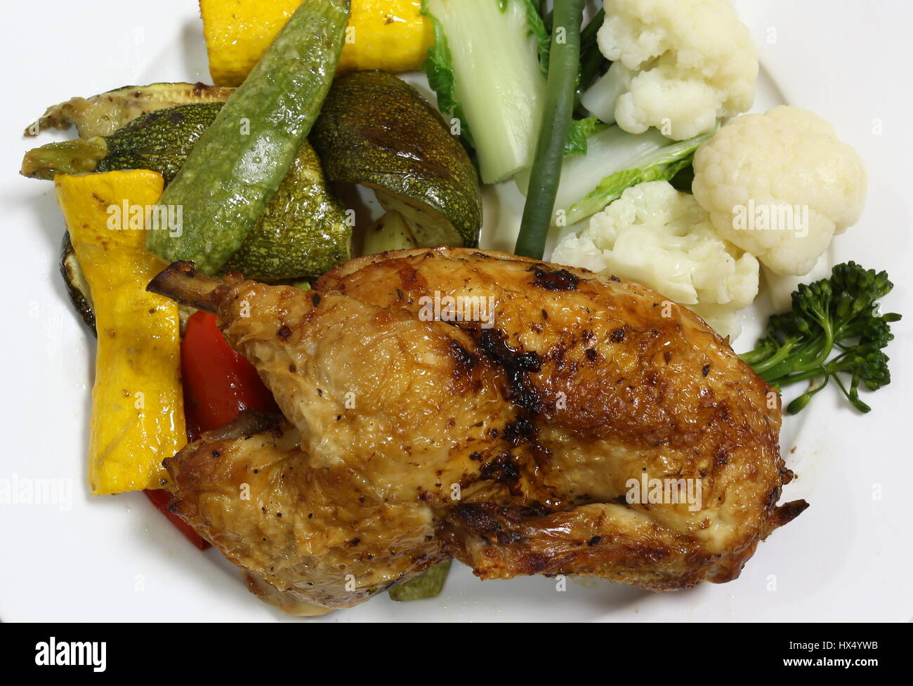 Half a grilled chicken served with grilled courgettes and bell pepper and steamed sprouting broccoli and cauliflower Stock Photo