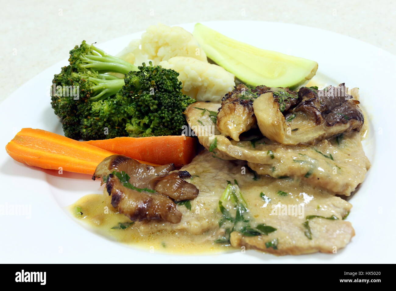 Slices of veal and oyster mushrooms in a creamy sauce with steamed carrots, cauliflower, courgette and broccoli, side view Stock Photo