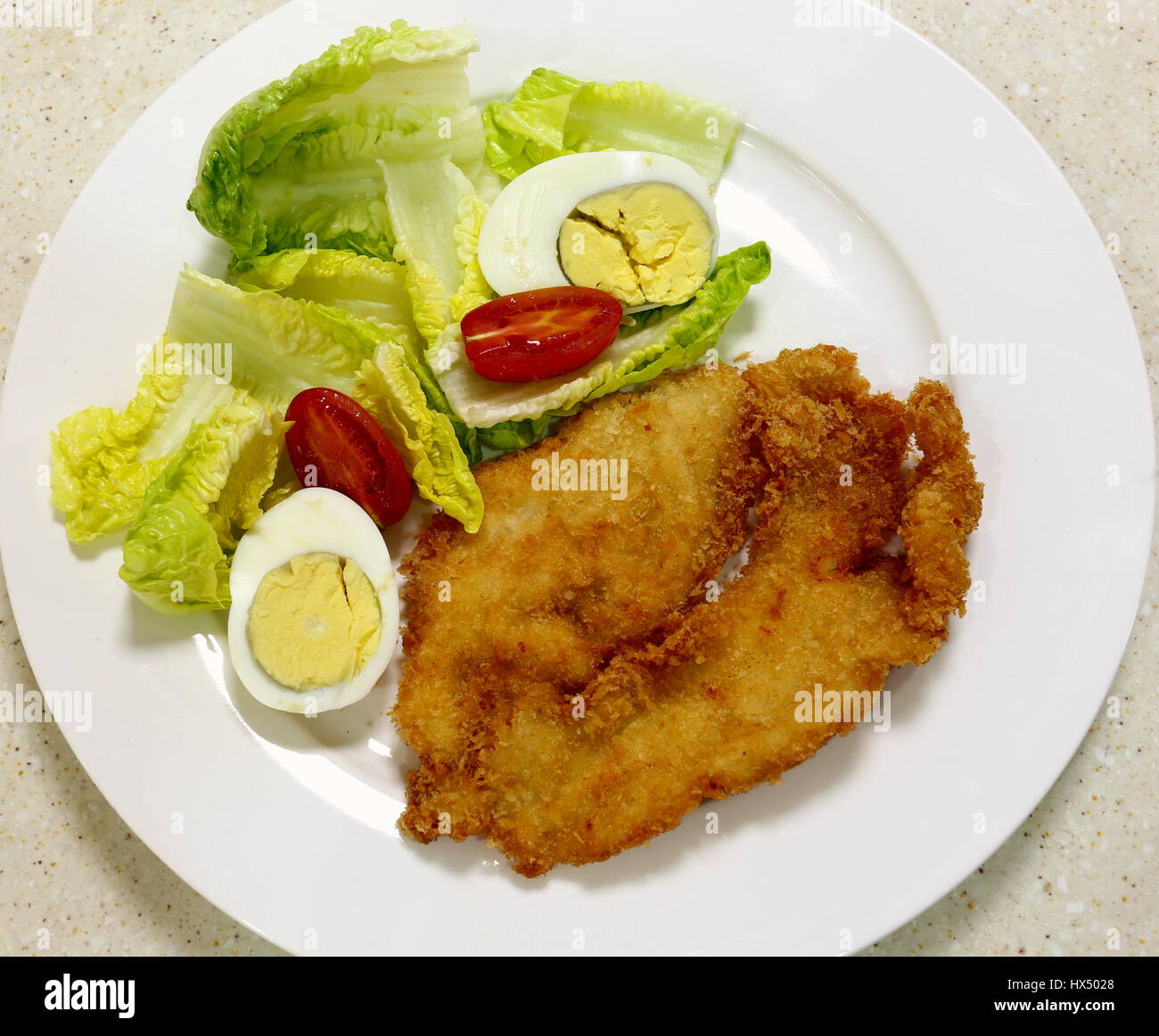 Breaded chicken breast fillet with a salad of lettuce, tomato and hard-boiled egg, top view Stock Photo