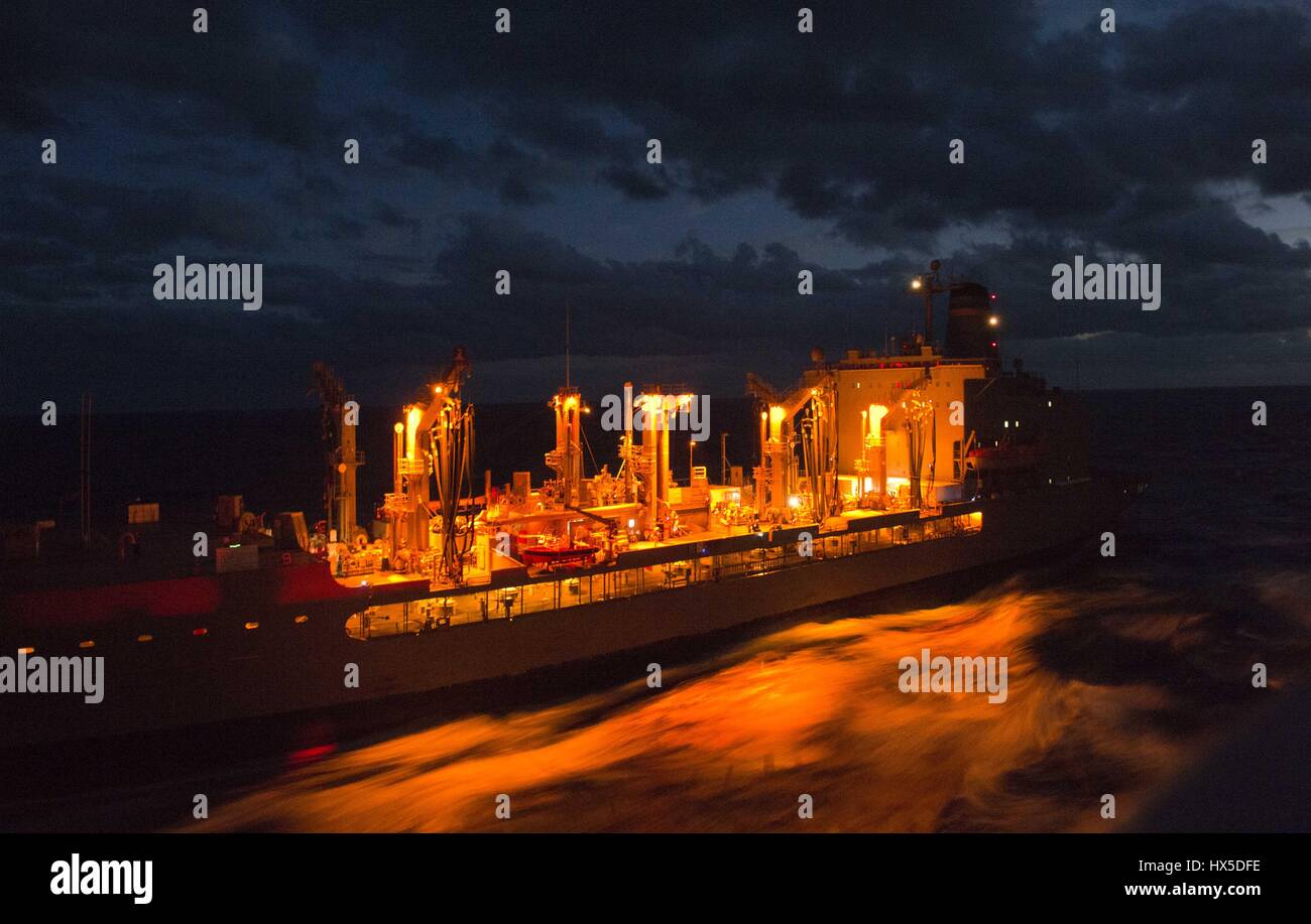 Lit with a fiery glow in the night, Military Sealift Command fleet replenishment oiler USNS Leroy Grumman (T-AO 195) charges along in the vast Atlantic Ocean, February 10, 2013. Image courtesy US Navy. Stock Photo