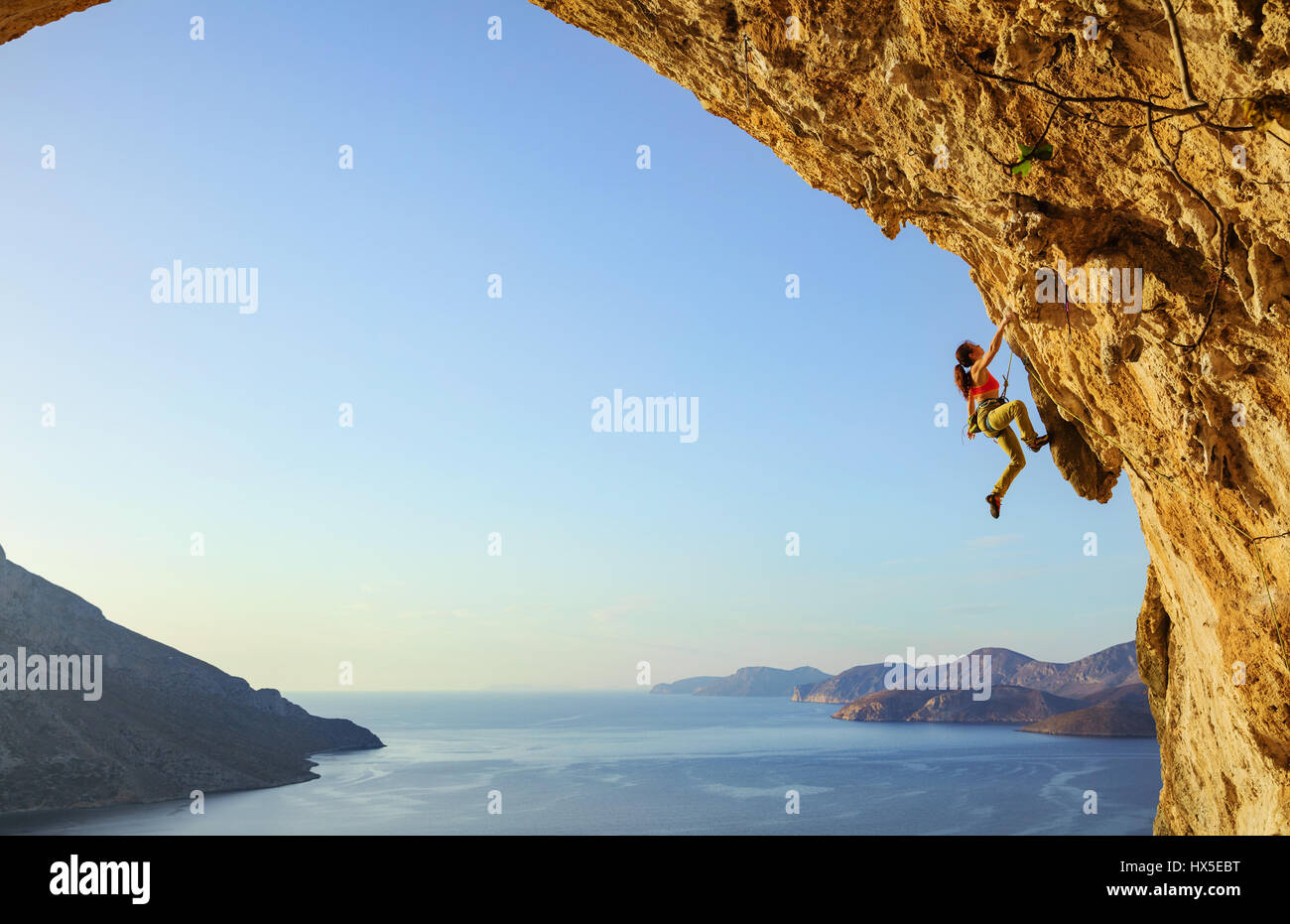 Young woman climbing challenging route in cave at sunset, Kalymnos island, Greece Stock Photo