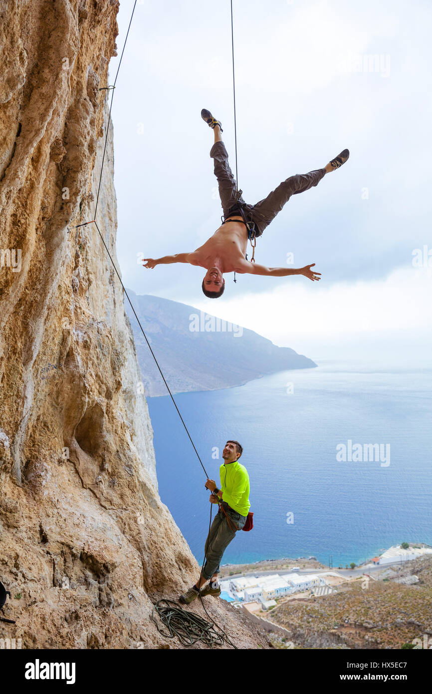 Rock climbers fooling around: one man hanging upside down while being lowered, belayer watching him and smiling Stock Photo