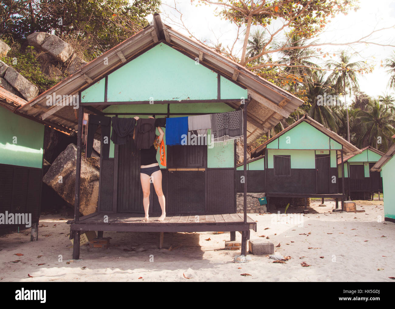 Woman hanging clothes to dry outside bungalow on a beach in Thailand. Stock Photo