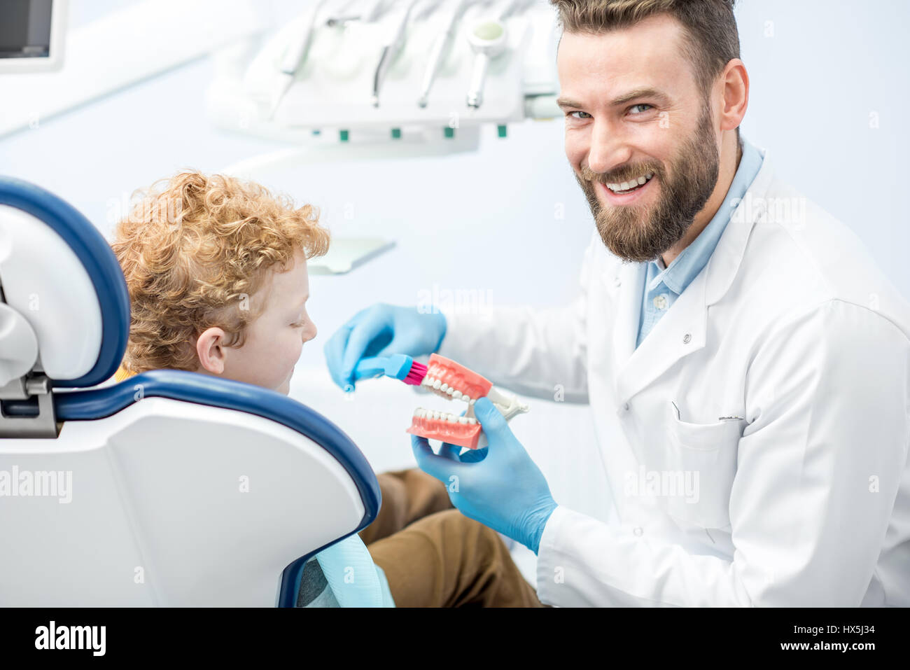 Dentist showing the boy how to brush teeth on artificial jaw at the