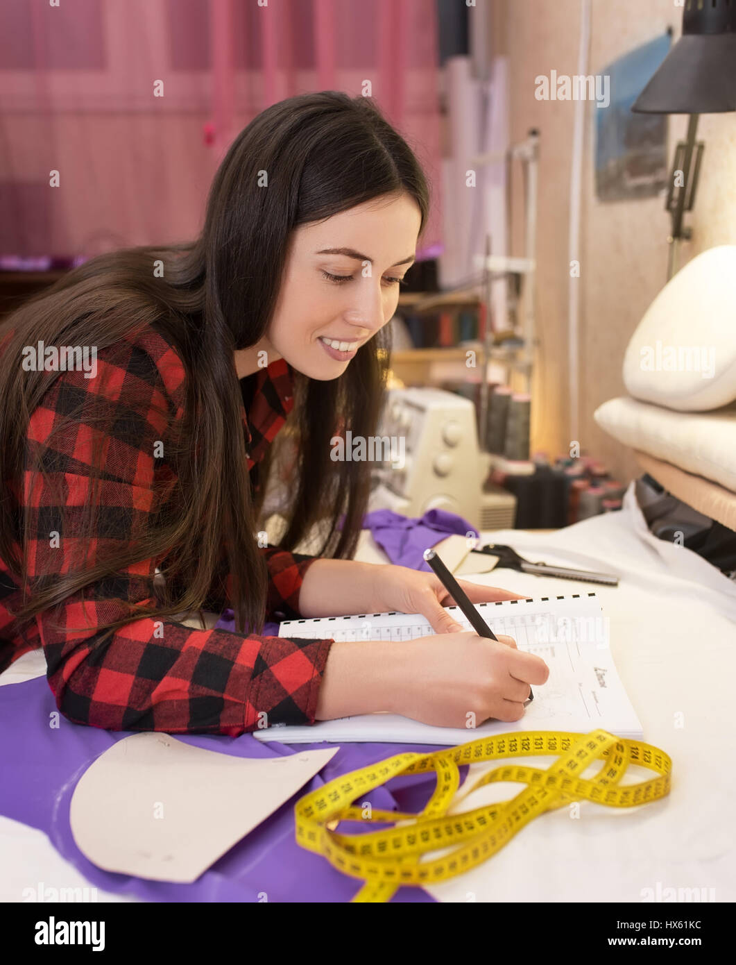 young woman seamstress making notes at notebook. Fashion designer drawing sketches. Hobby sewing as a small business concept. Tailor measuring and wri Stock Photo