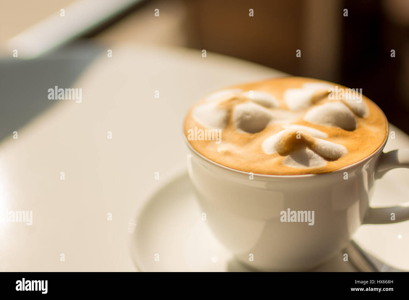 A latte coffee with decorative froth in  white cup at golden hour with selective focus. Stock Photo