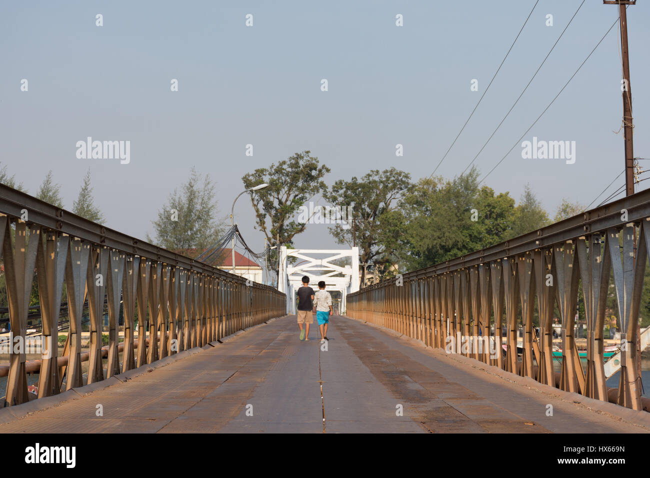 the backs of two children walking away across a metal river crossing bridge in Cambodia. Stock Photo