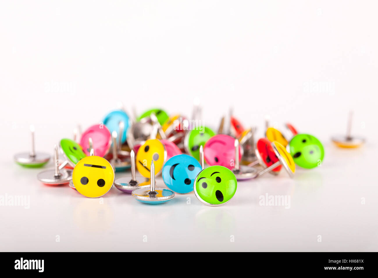 Pile of colorful smiley pushpins on a white surface. Pile of smiley thumbtacks isolated on white background. Stock Photo